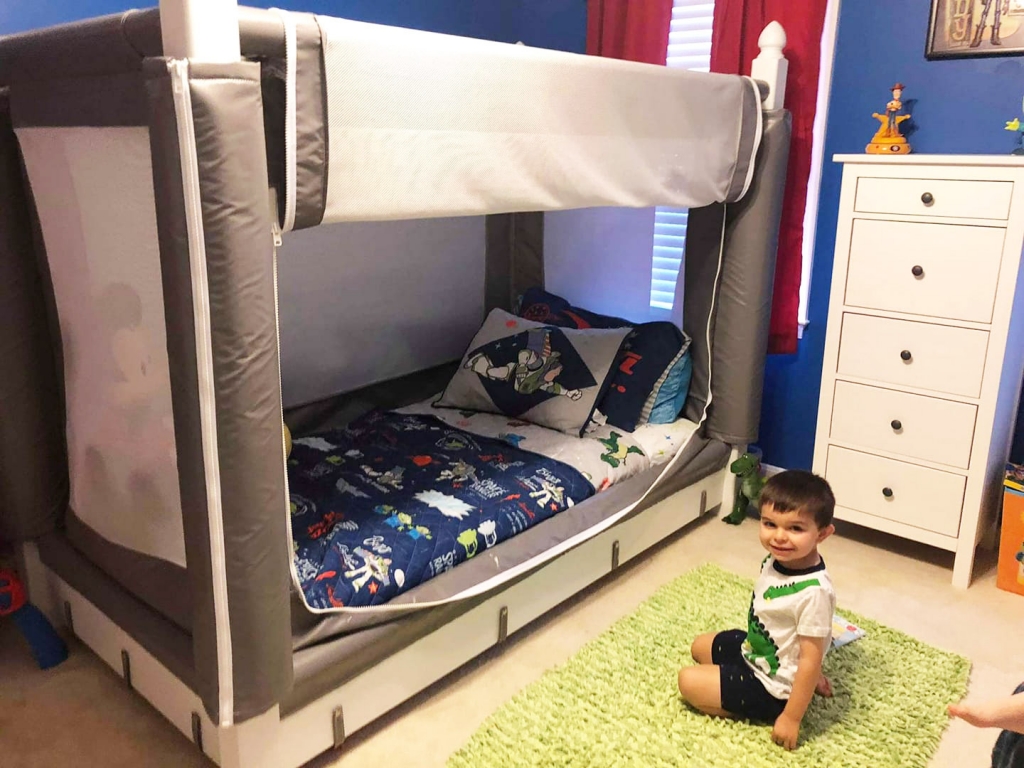 A child playing on a green rug next to a Noah's World safety bed in their bedroom